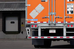 Orange and white International flatbed truck backed up to loading dock with caution sign visible