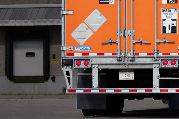 Orange and white International flatbed truck backed up to loading dock with caution sign visible