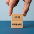 Hand stacking wooden blocks labeled 'SAFE' and 'UNSAFE' against a blue background, representing decision-making and risk assessment.