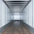 Empty cargo trailer interior with white walls, overhead lighting, and wooden floor