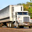White refrigerated semi-truck with Thermo King cooling unit parked on roadside with trees and red car visible