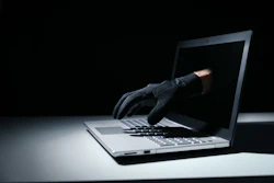 Gloved hand reaching through laptop screen in dark setting, representing cybersecurity threat or digital crime