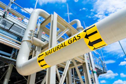 Industrial natural gas pipeline with yellow and black warning stripes against blue sky and industrial facility structure