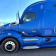Bright blue Peterbilt semi-truck with company branding parked in industrial lot under clear sky