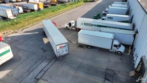 Aerial view of commercial truck yard with multiple white delivery trucks and trailers parked in organized rows on asphalt