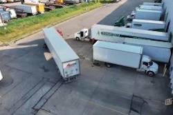 Aerial view of commercial truck yard with multiple white delivery trucks and trailers parked in organized rows on asphalt
