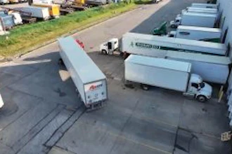 Aerial view of commercial truck yard with multiple white delivery trucks and trailers parked in organized rows on asphalt