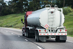 White tanker truck traveling on highway with green hillside landscape in background
