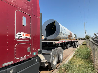 Red semi-truck cab with tanker trailer on rural road under clear sky