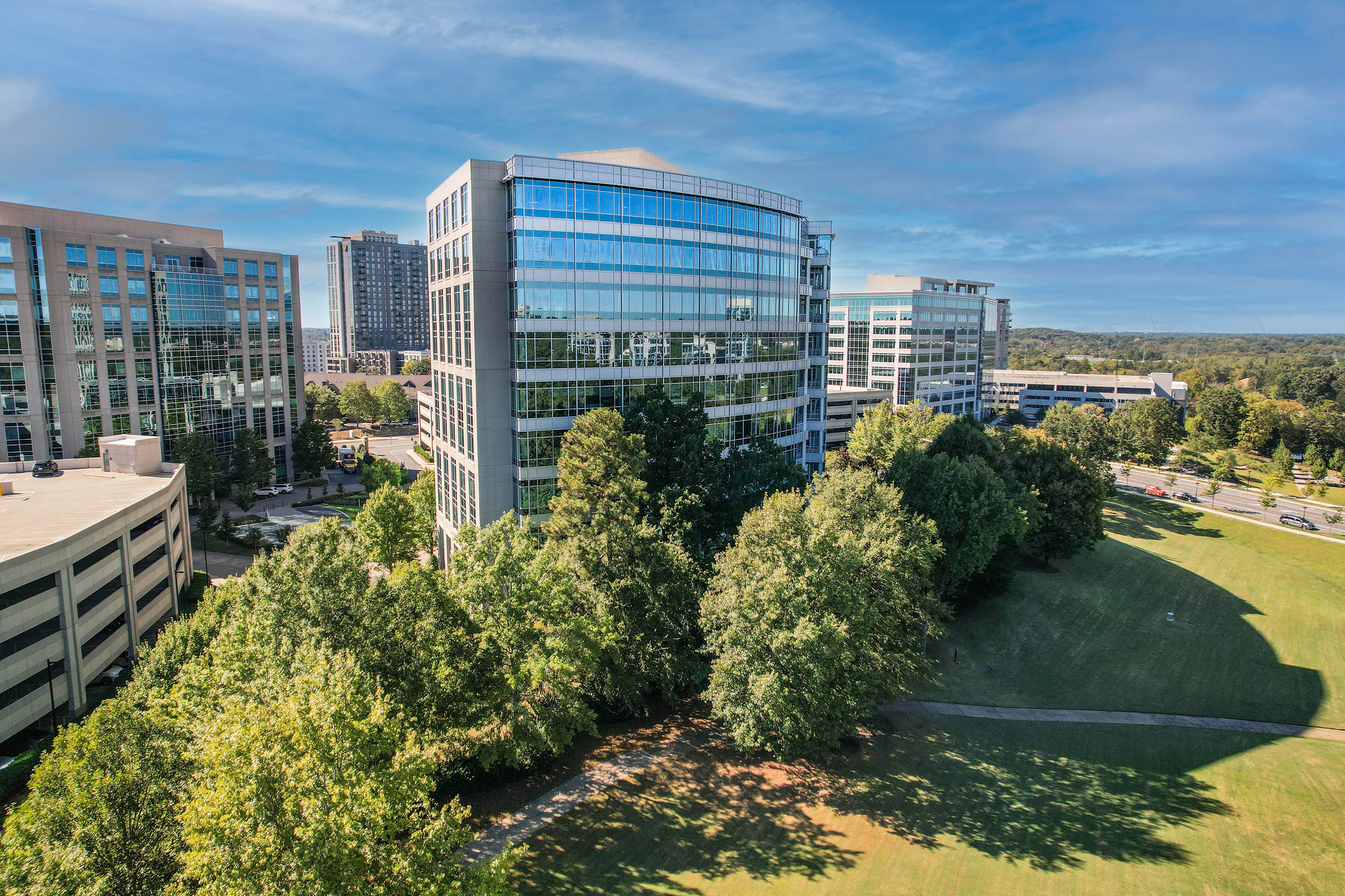 Aerial view of modern corporate campus with glass office buildings, green lawn, and mature trees under blue sky