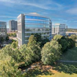 Aerial view of modern corporate campus with glass office buildings, green lawn, and mature trees under blue sky