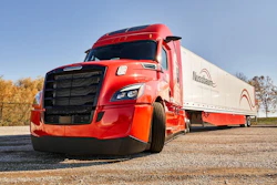 Red Nussbaum semi-truck with white refrigerated trailer parked on gravel lot
