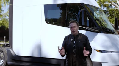 Man gesturing in front of white Tesla Semi truck outdoors