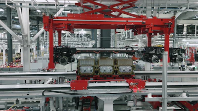 Red overhead crane system with engine components on assembly line in automotive manufacturing facility