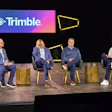 Four business professionals participate in a panel discussion on stage beneath a Trimble company logo backdrop with yellow geometric design elements.
