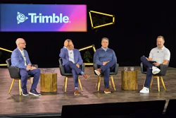 Four business professionals participate in a panel discussion on stage beneath a Trimble company logo backdrop with yellow geometric design elements.
