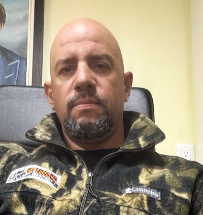 Bald man with goatee wearing camouflage Columbia jacket in indoor setting