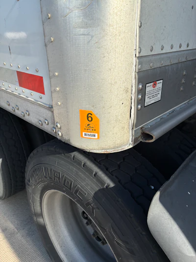 Close-up of industrial trailer with riveted metal panels, tire, and hazard identification labels including orange number 6 marker