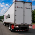 Truck-lite branded white commercial delivery truck with red logo and safety warning lights on highway