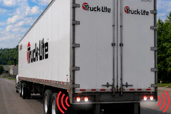 Truck-lite branded white commercial delivery truck with red logo and safety warning lights on highway