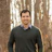 Smiling man in dark sweater and checkered shirt standing in a forest with bare trees Headshot