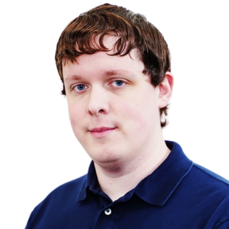 Professional headshot of a person with brown hair wearing a dark blue polo shirt against a white background Headshot