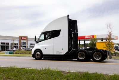 White semi-truck with black accents parked at commercial facility with Penske signage visible