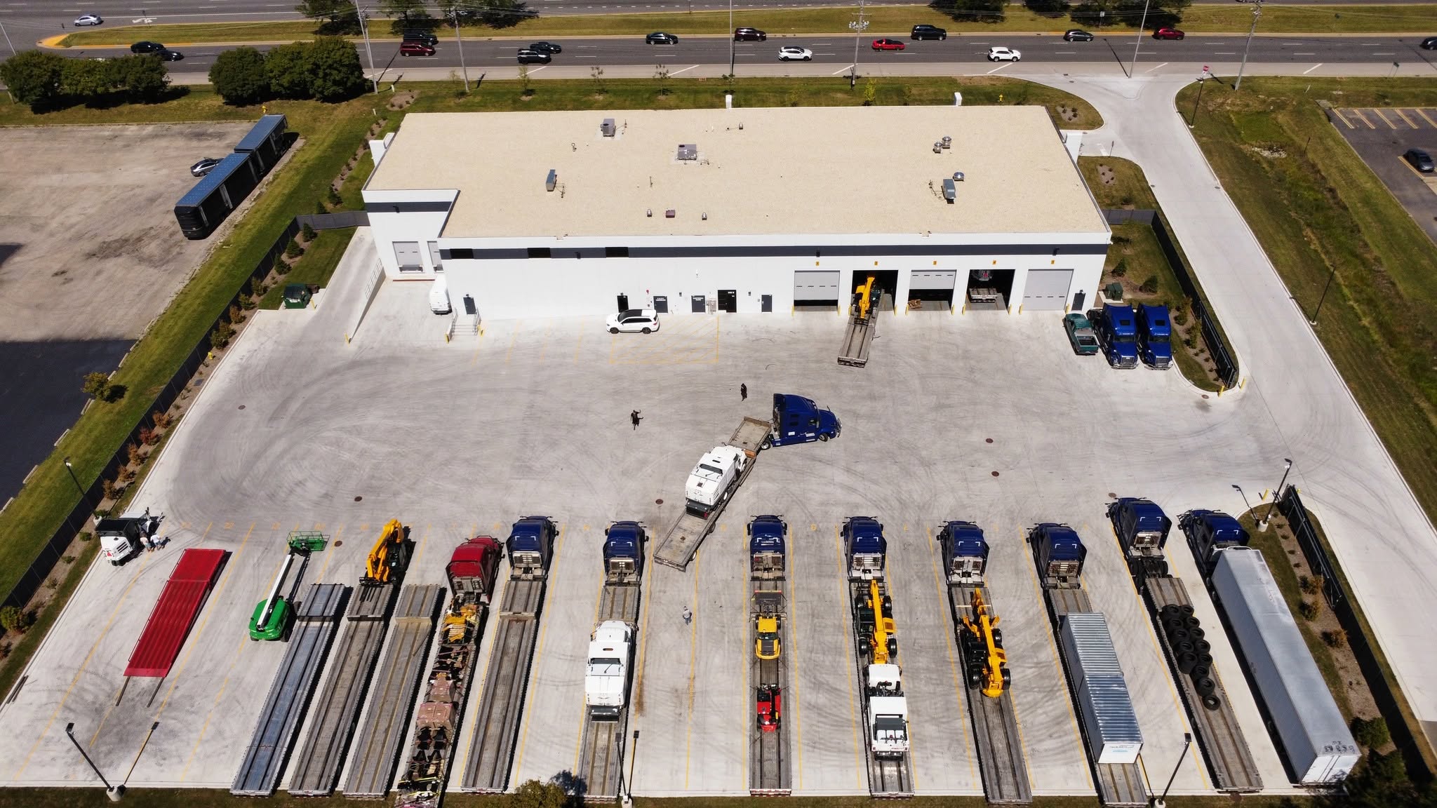 Aerial view of industrial warehouse facility with parking lot containing multiple commercial vehicles and equipment