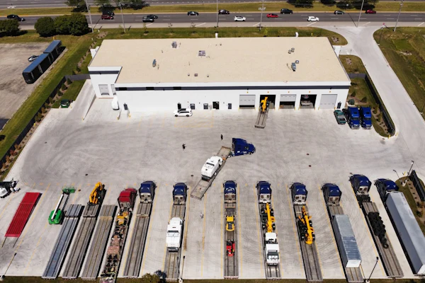 Aerial view of industrial warehouse facility with parking lot containing multiple commercial vehicles and equipment