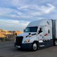 White and blue semi-truck with trailer parked on desert highway with rocky hills in background