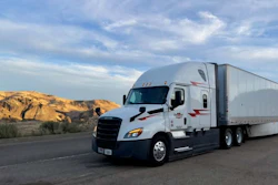 White and blue semi-truck with trailer parked on desert highway with rocky hills in background