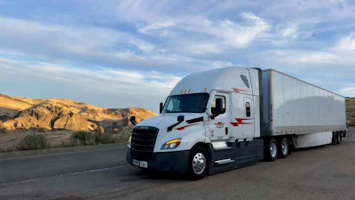 White and blue semi-truck with trailer parked on desert highway with rocky hills in background