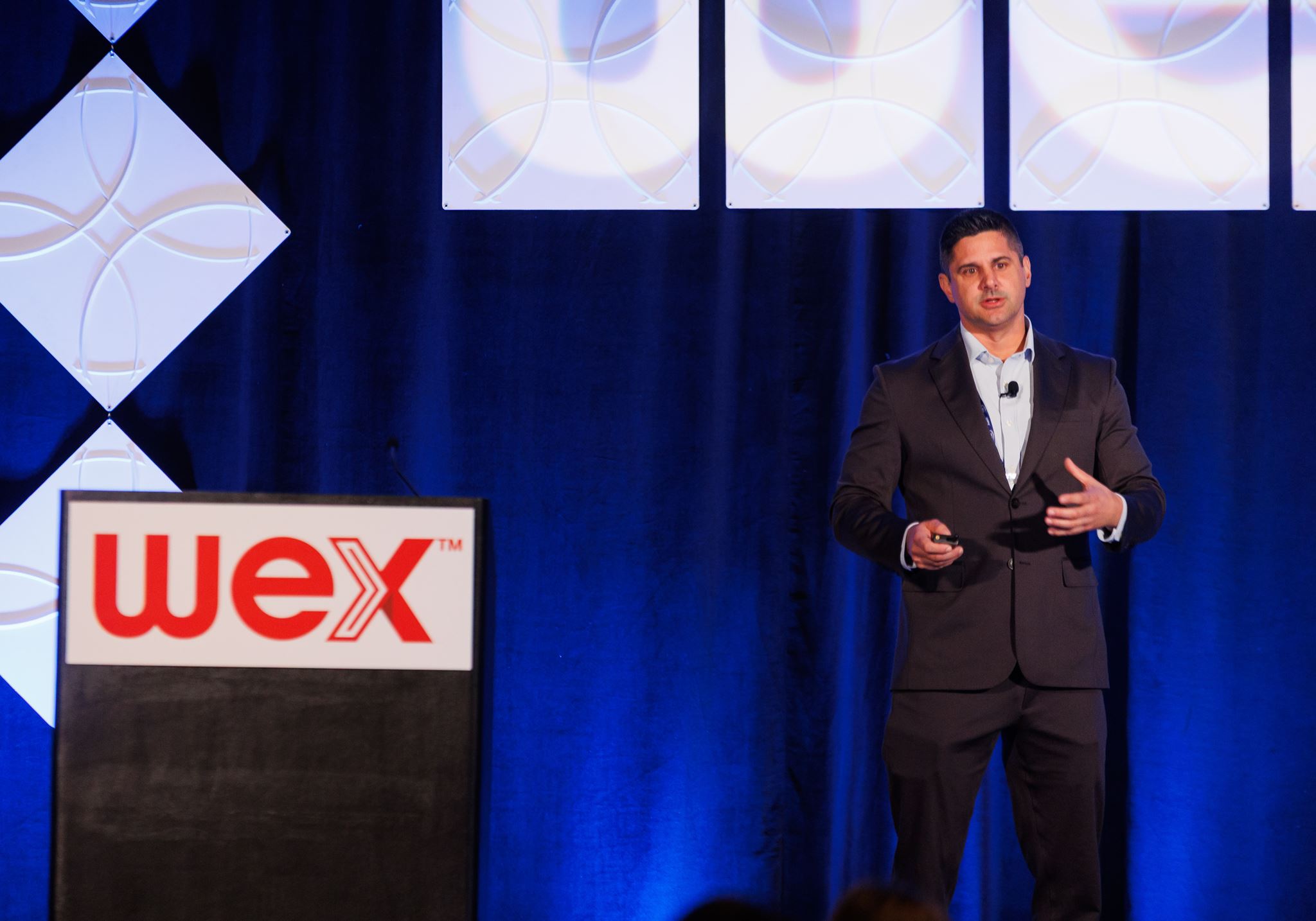 Professional speaker presenting at WEX corporate event on stage with branded podium