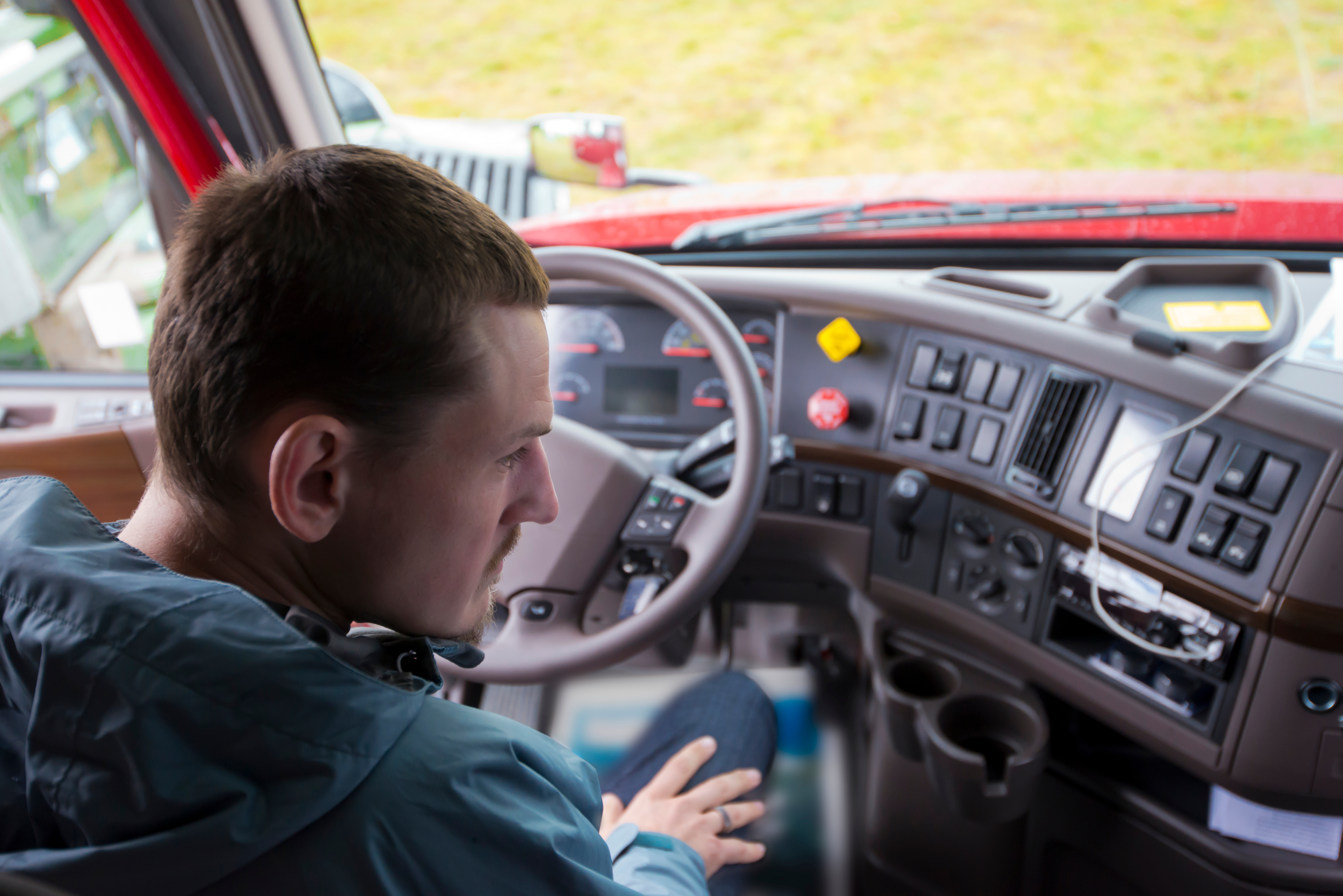 Truck driver at steering wheel inside cab of red commercial vehicle