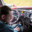 Truck driver at steering wheel inside cab of red commercial vehicle