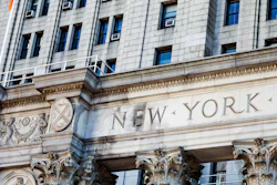 Ornate stone building facade with 'NEW YORK' carved text and classical Corinthian columns