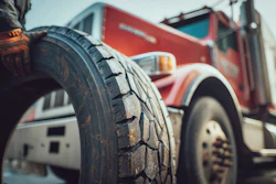 Close-up of worn truck tire tread with red commercial truck blurred in background