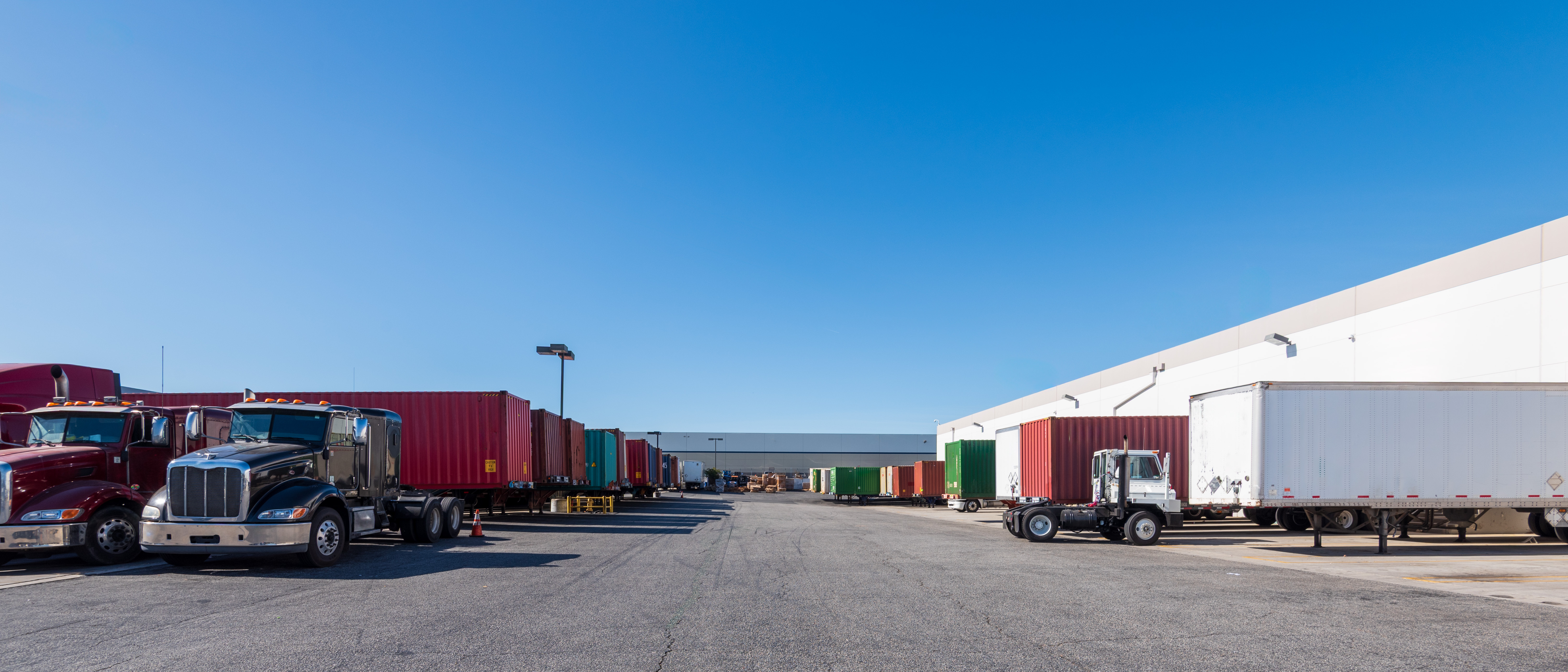Industrial logistics yard with semi-trucks and colorful shipping containers under clear blue sky
