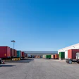 Industrial logistics yard with semi-trucks and colorful shipping containers under clear blue sky