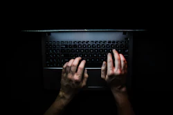 Hands typing on a laptop keyboard viewed from above in low lighting