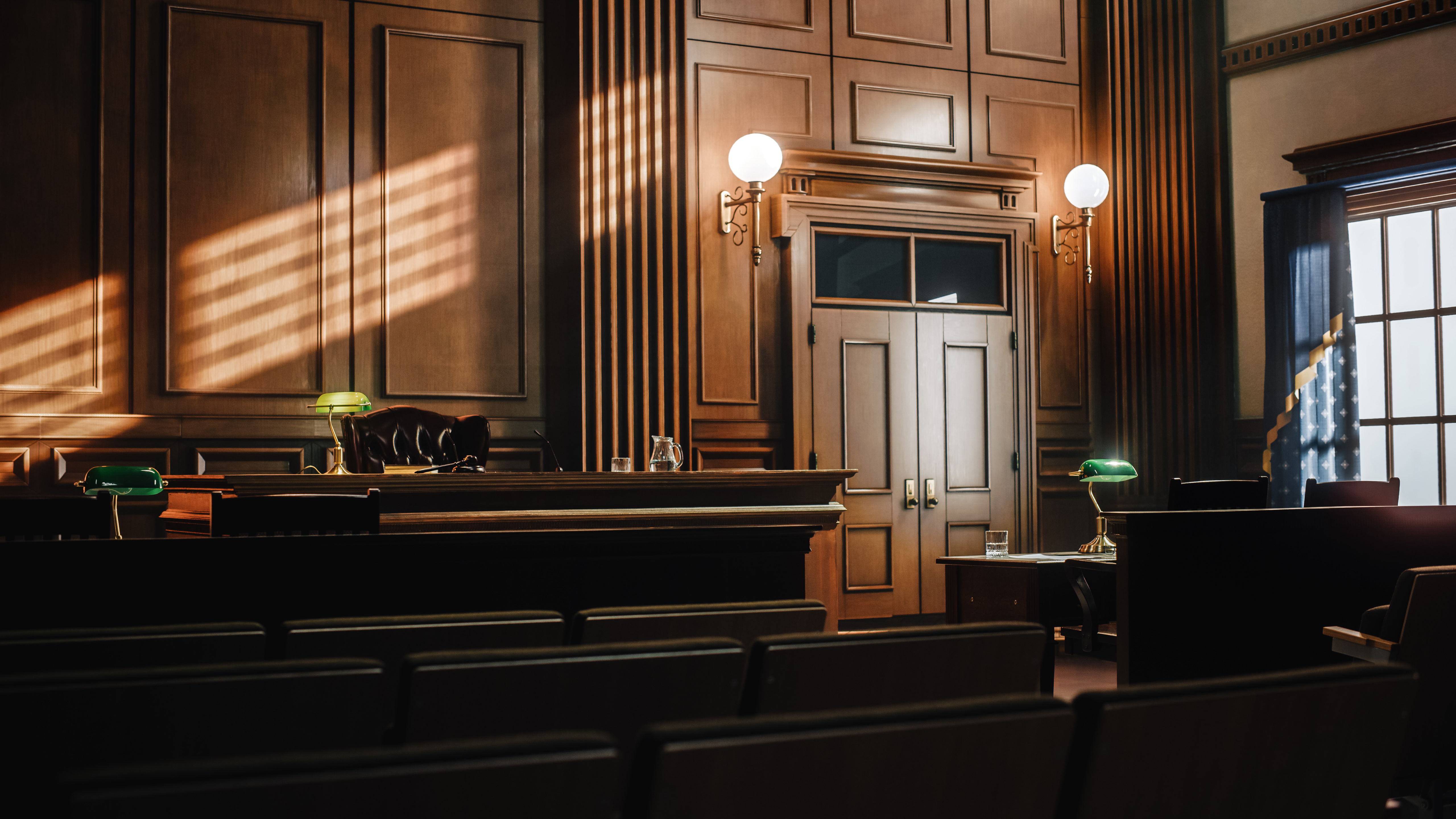 Empty courtroom with wooden paneling, judge's bench, jury box, and period lighting fixtures