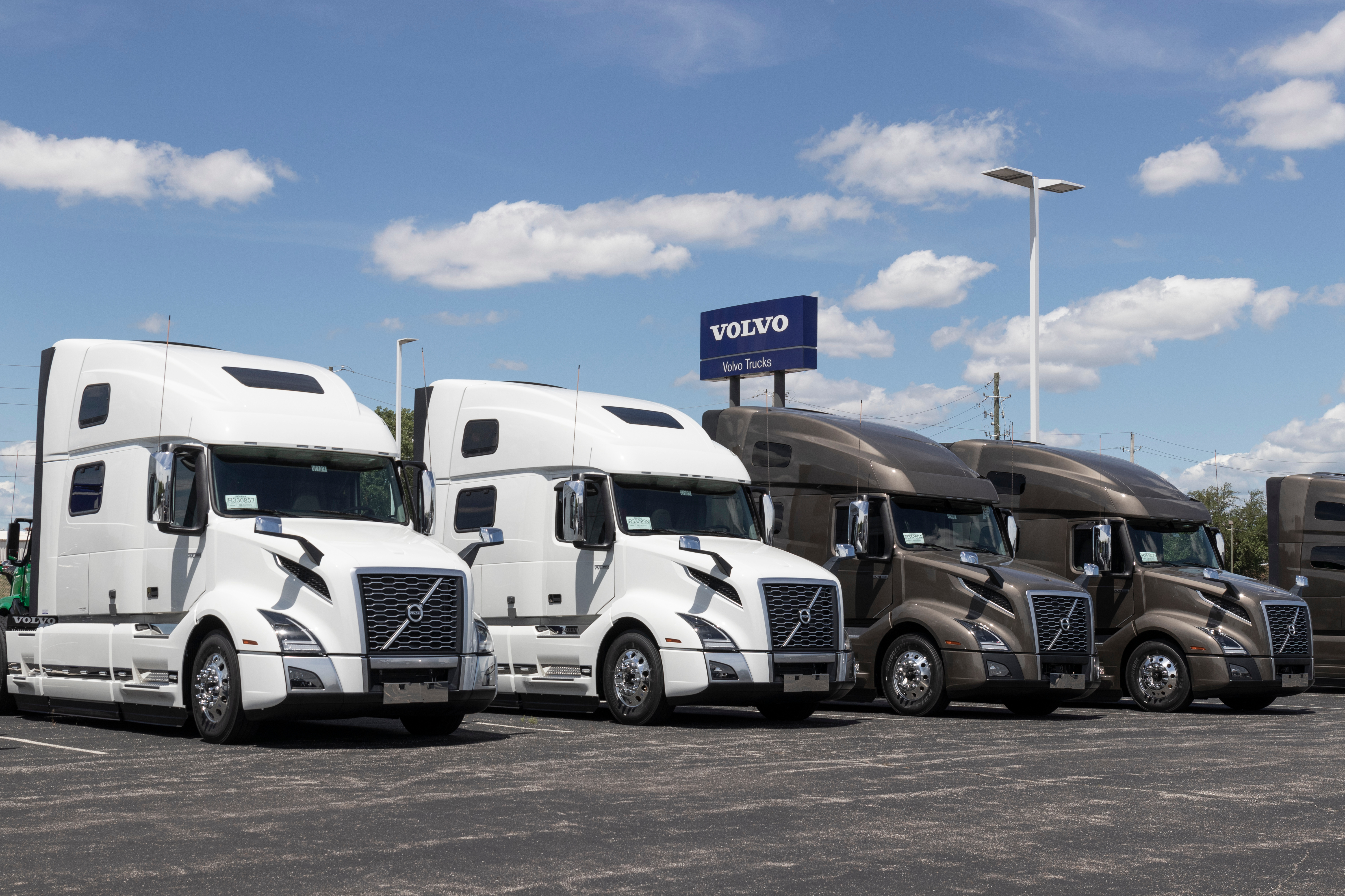 Row of white and brown Volvo semi-trucks parked at a dealership lot under blue sky