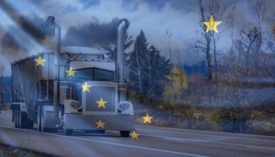 White semi-truck with yellow stars driving through a barren landscape under a cloudy blue sky