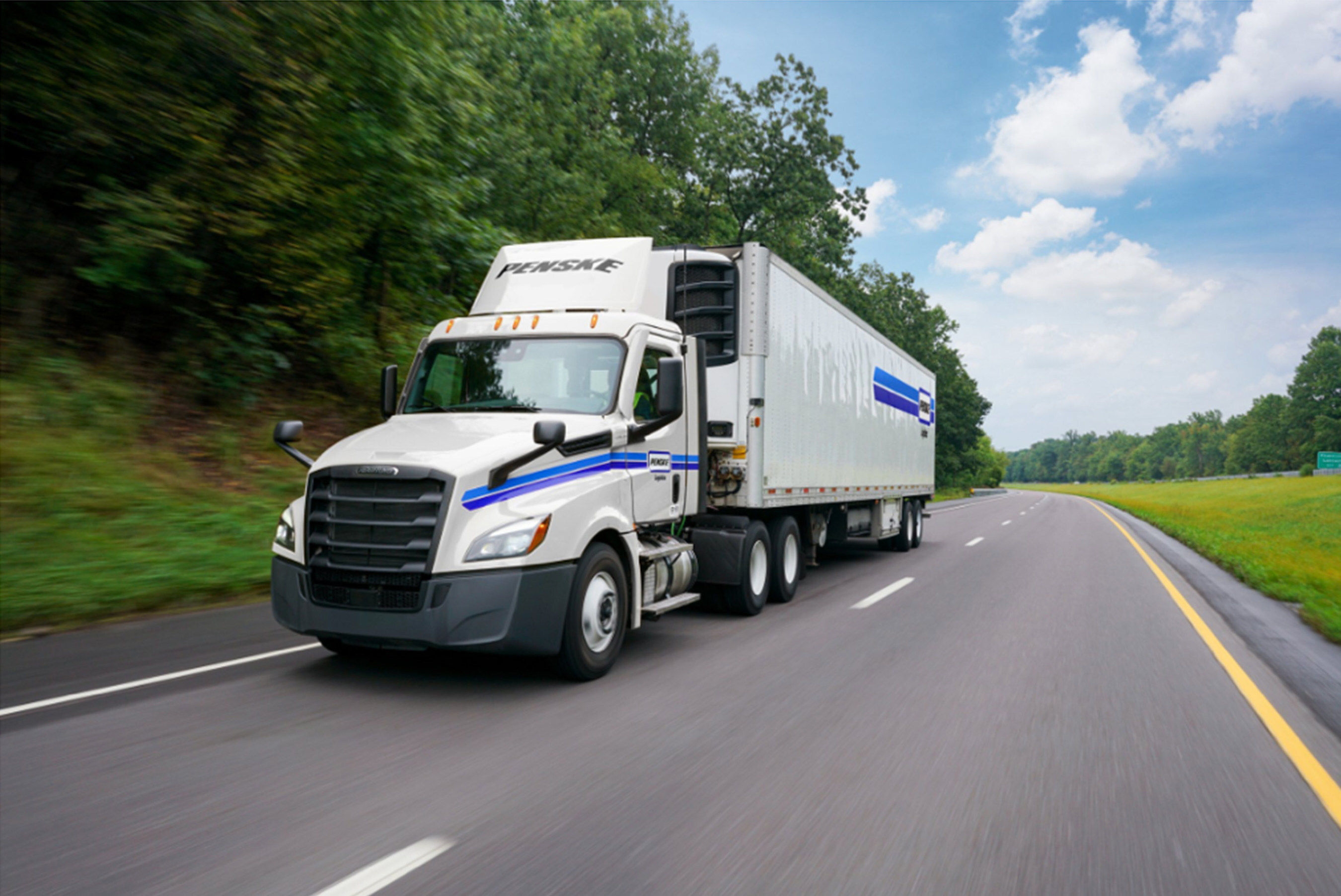 White Prestige semi-truck with blue stripe driving on highway through green landscape