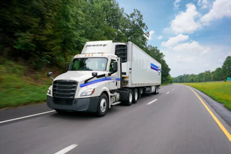 White Prestige semi-truck with blue stripe driving on highway through green landscape