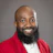 Professional headshot of a smiling man wearing a red blazer and white shirt against a gray background Headshot