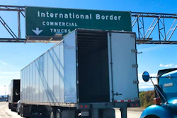 Green highway sign directing commercial trucks to International Border with downward arrow