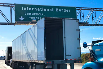 Green highway sign directing commercial trucks to International Border with downward arrow
