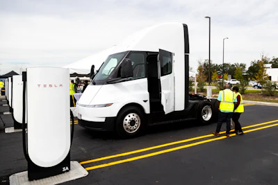 Tesla Semi truck charging at a Supercharger station with worker in safety vest