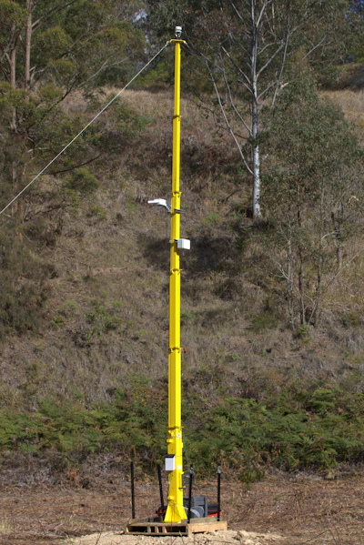 Tall yellow utility pole with guy-wires in forested hillside terrain